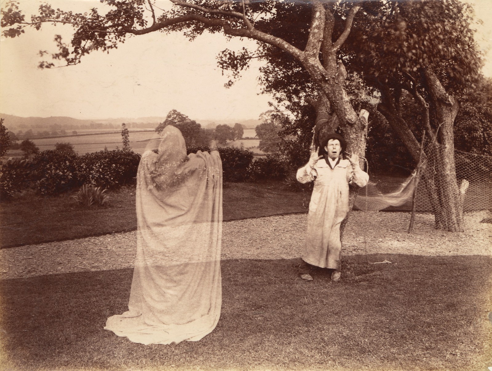 A Victorian double exposure photograph of a ghost in a white sheet frightening a man in a smock, c. 1887.